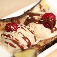 Image of A split caramelized banana with two scoops of coconut banana ice cream and topped with raspberries and chocolate fudge 