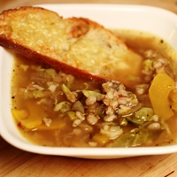 Image of A bowl of caramelized onion & delicata soup with farro and a toasted piece of bread